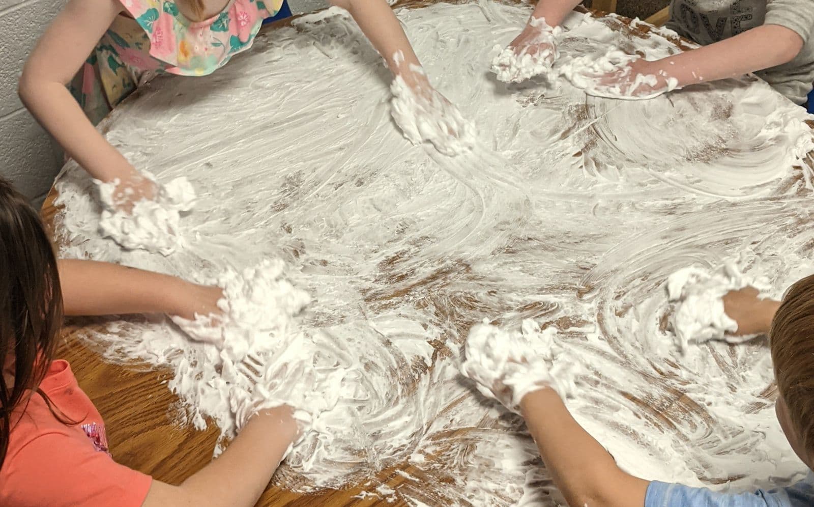 Preschoolers’ hands spreading shaving cream across a classroom table
