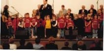 An early NNS Christmas program, with children in red shirts singing on the church stage
