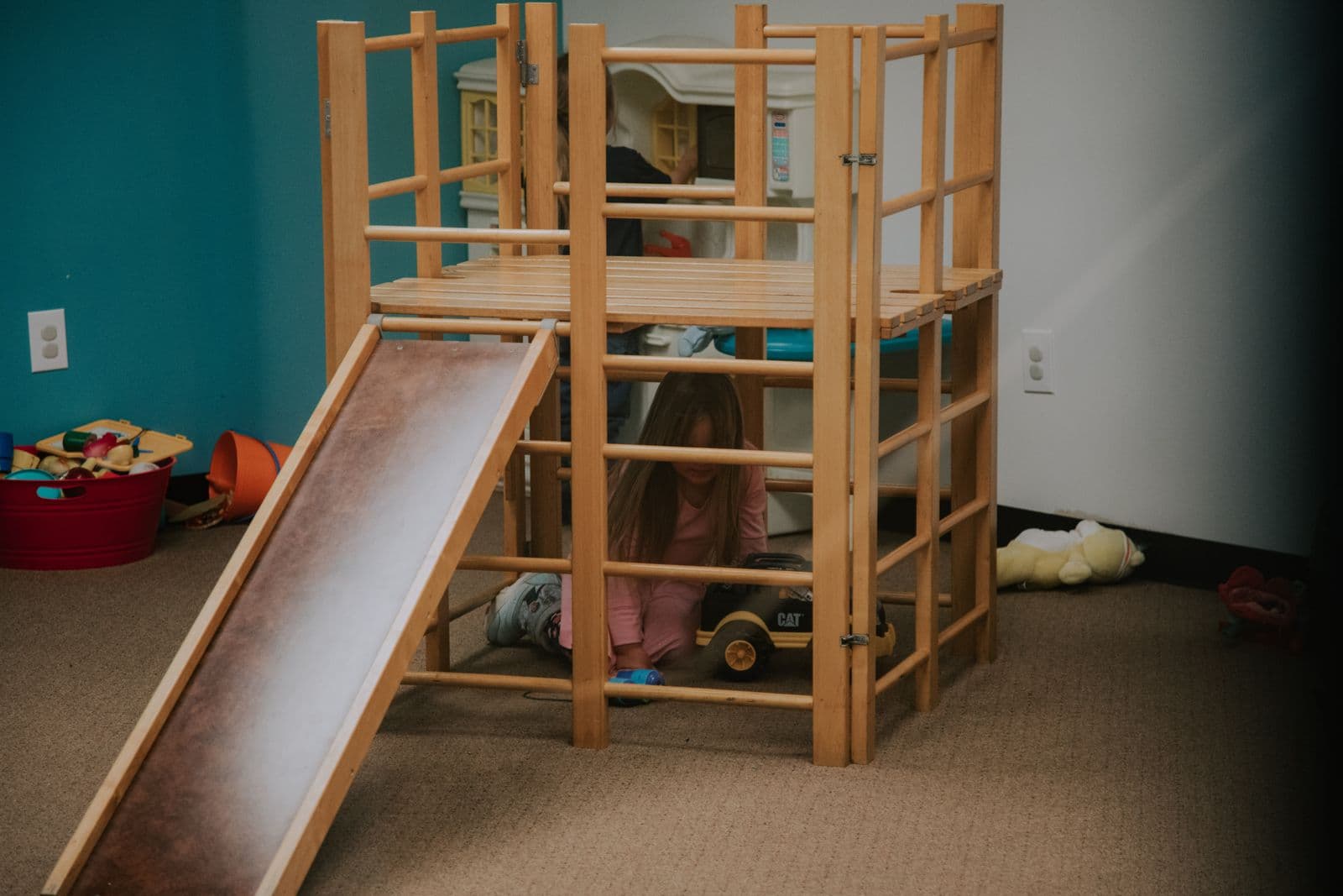 A wooden play loft with a slide in a preschool classroom